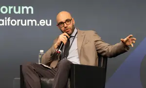 Jacopo Perfetti, calvo e con occhiali, parla al microfono durante un evento AIForum, gesticolando con la mano.