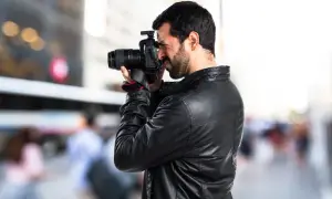 Un fotoreporter con giacca di pelle cattura un momento in strada, mostrando il vero significato del suo mestiere: documentare la realtà.
