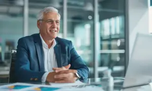 Un uomo anziano con capelli grigi e occhiali, vestito con giacca blu, sorride mentre discute di affari. Potrebbe essere il CFO che spiega i risultati finanziari.