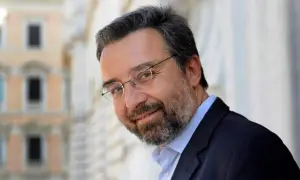 Marco Damilano, giornalista con barba e occhiali, sorride con un blazer scuro.