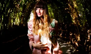 Chiara Tagliaferri, con un tailleur rosa e un fiore sul petto, posa in un tunnel di bambù illuminato dal sole.