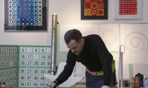 Adriano Attus, artista, disegna cerchi colorati su una tela nera. Sullo sfondo, opere astratte e numeri.
