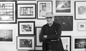 Denis Curti, circondato da opere fotografiche, sorride con le braccia conserte.