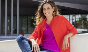 Francesca Bria sorride, seduta all'esterno con un cardigan arancione acceso e una maglia fucsia.