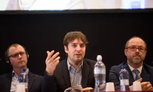 Beniamino Pagliaro parla a un microfono, con altri due uomini seduti al suo fianco.