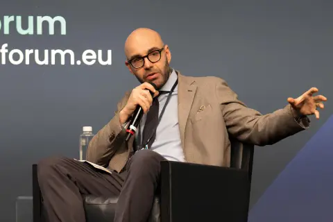 Jacopo Perfetti, calvo e con occhiali, parla al microfono durante un evento AIForum, gesticolando con la mano.