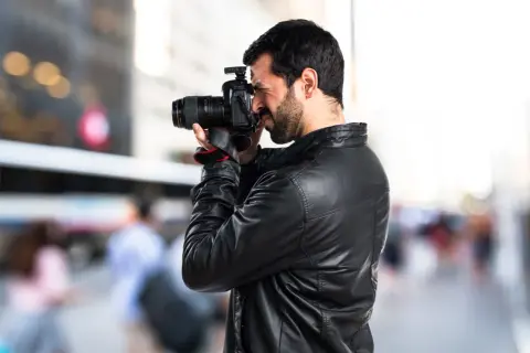 Un fotoreporter con giacca di pelle cattura un momento in strada, mostrando il vero significato del suo mestiere: documentare la realtà.