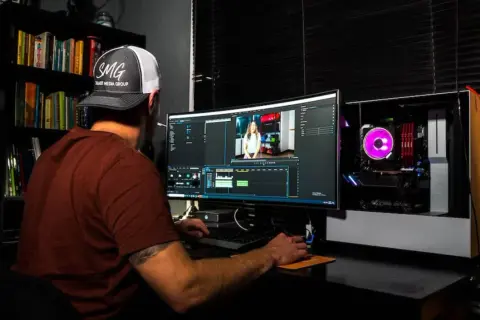 Uomo con cappellino SMG impegnato in un corso di editing video, lavora su un computer con software di montaggio.