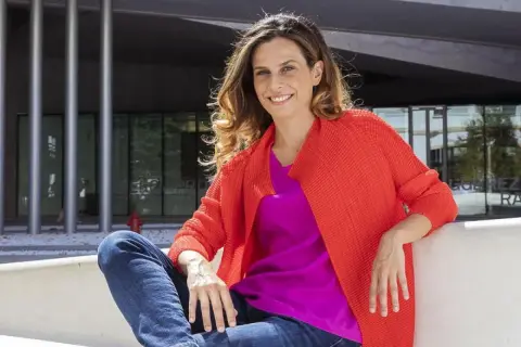 Francesca Bria sorride, seduta all'esterno con un cardigan arancione acceso e una maglia fucsia.