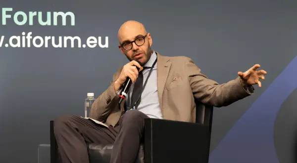 Jacopo Perfetti, calvo e con occhiali, parla al microfono durante un evento AIForum, gesticolando con la mano.