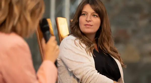 Martina Carone, con capelli castani e un cardigan beige, ascolta attentamente durante un'intervista.