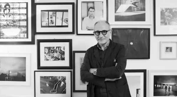 Denis Curti, circondato da opere fotografiche, sorride con le braccia conserte.