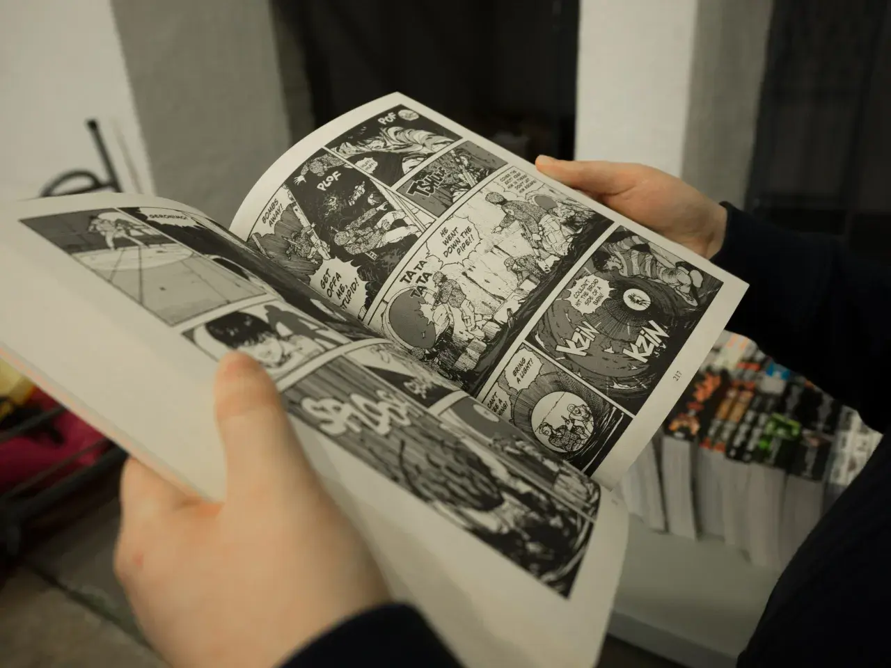 Mani che sfogliano un libro di graphic journalism con scene d'azione e dialoghi in stile fumetto.