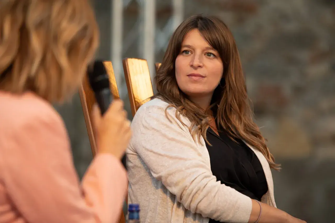 Martina Carone, con capelli castani e un cardigan beige, ascolta attentamente durante un'intervista.