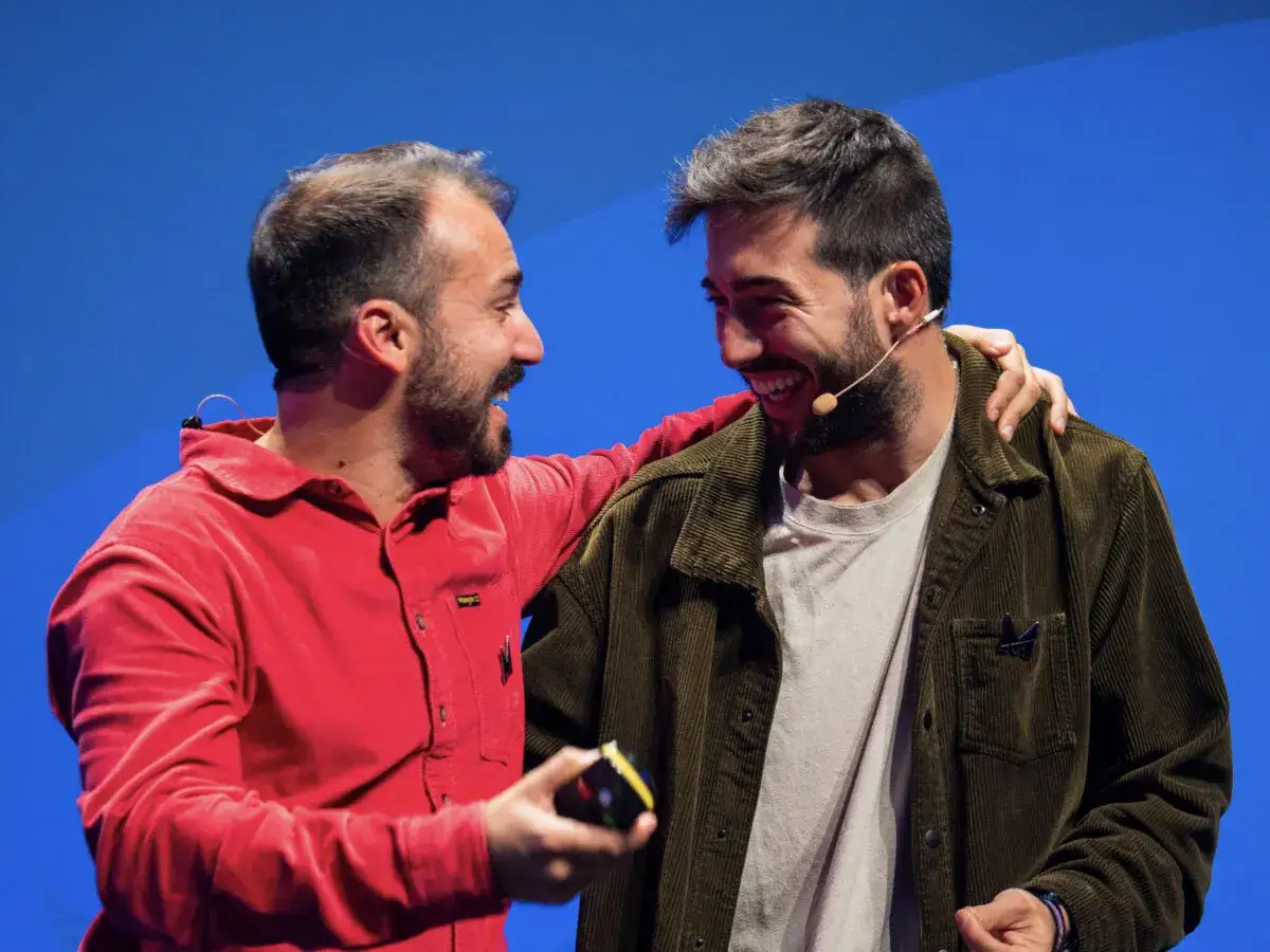 Dario Vignali e un altro marketer ridono sul palco, con un microfono e un sorriso contagioso.