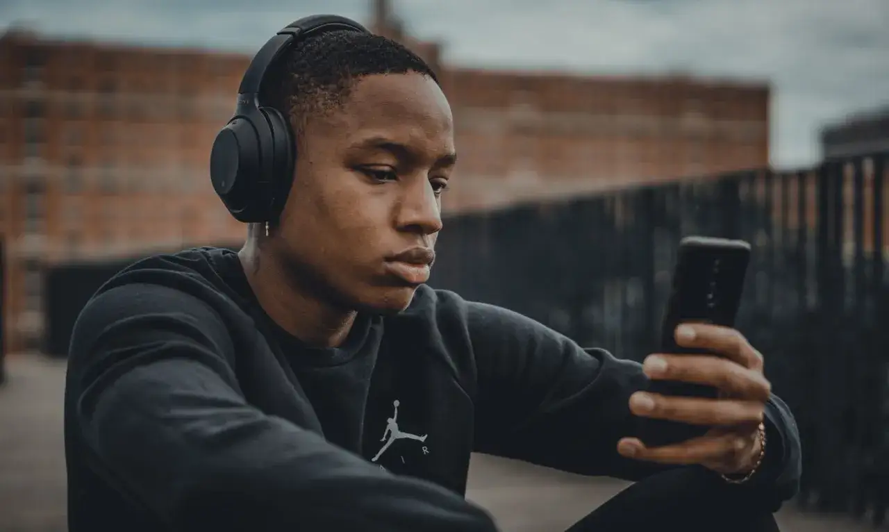 Giovane con cuffie nere e smartphone, pronto dove ascoltare podcast.