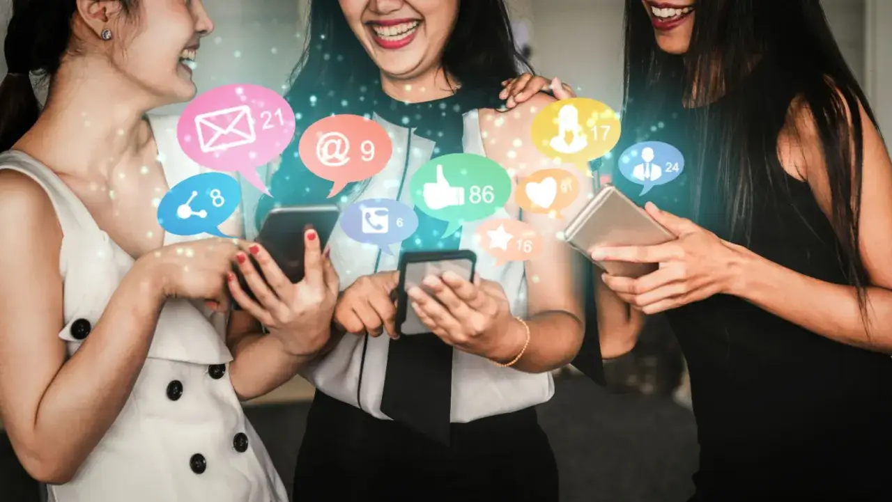 Tre amiche sorridono, immerse nei loro smartphone, circondate da icone social che simboleggiano l'audience engagement e la connessione digitale.