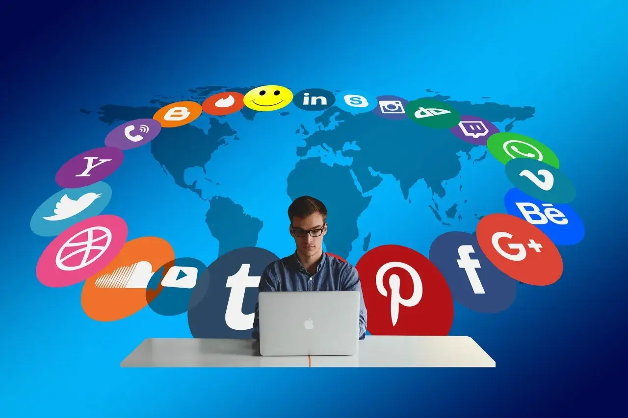 Giovane uomo al computer, circondato da icone social, simboleggia il mondo del web journalism e la connessione globale.