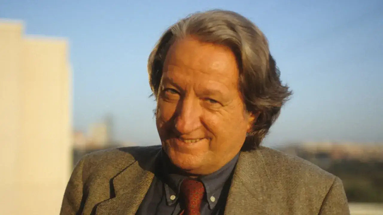 Ritratto di un giornalista storico con capelli grigi, indossa una giacca di tweed e una cravatta.