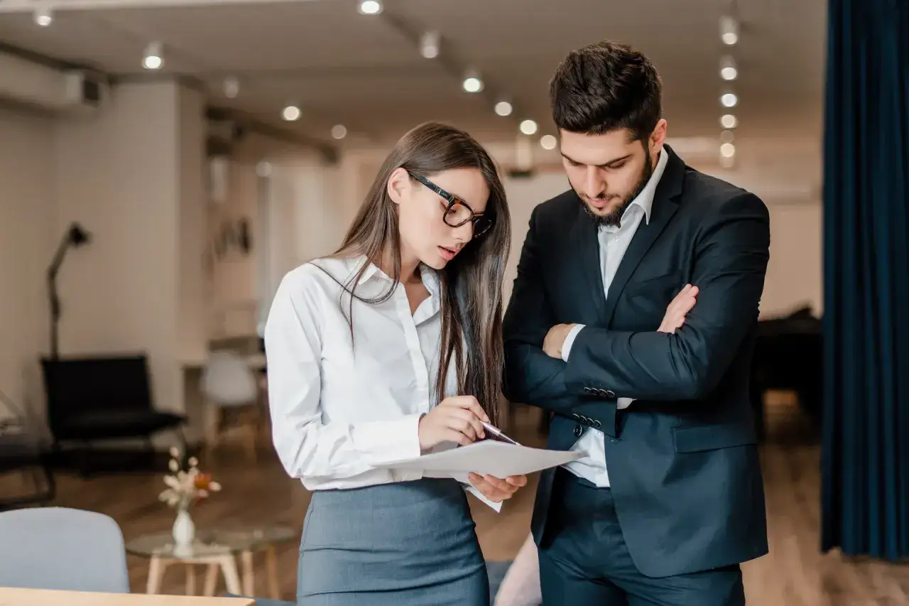 Uomo e donna discutono documenti in ufficio, pianificando un evento. Il loro codice ATECO per l'organizzazione eventi &egrave; fondamentale per il successo.