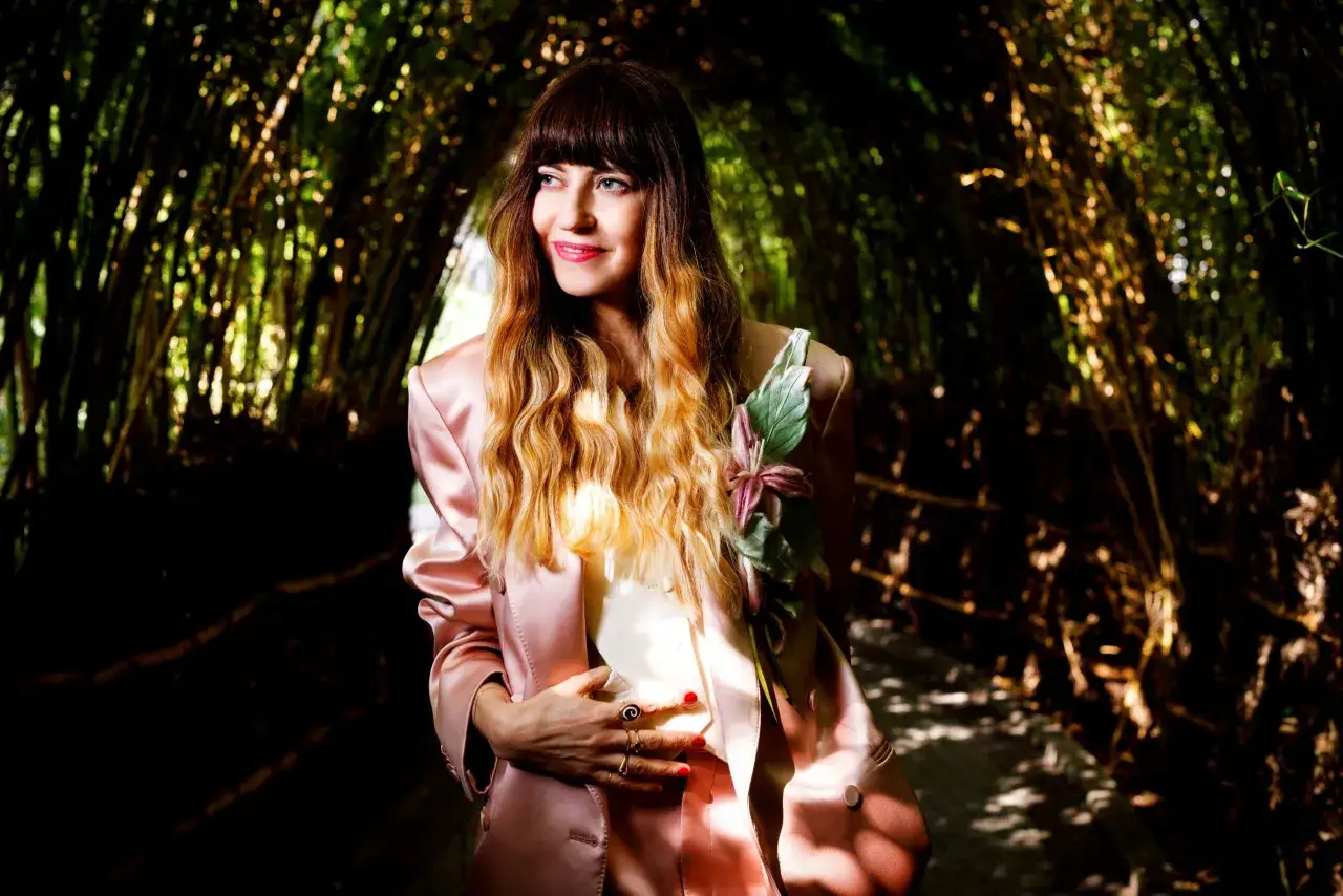 Chiara Tagliaferri, con un tailleur rosa e capelli biondi, posa in un tunnel di bambù illuminato dal sole.
