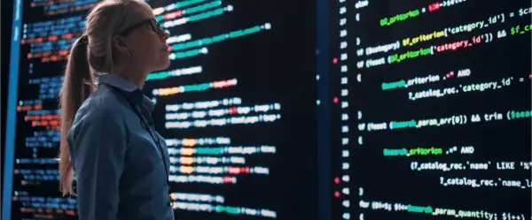 Donna con occhiali analizza codice su schermo luminoso, simbolo di un tim enterprise in evoluzione.