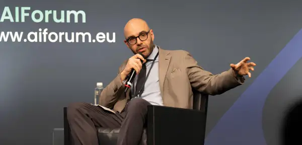 Jacopo Perfetti, calvo e con occhiali, parla al microfono durante un evento AIForum, gesticolando con la mano.