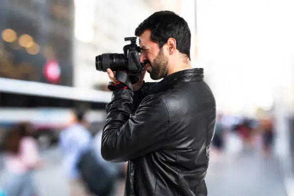Un fotoreporter con giacca di pelle cattura un momento in strada, mostrando il vero significato del suo mestiere: documentare la realtà.