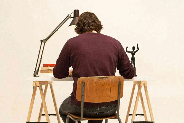 Uomo seduto alla scrivania, illuminato da una lampada, con libri e una statuetta. Il suo **titolo clickbait** è un mistero!