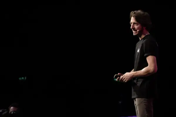 Un uomo con una maglietta nera con la lettera "M" parla sul palco, simile a uno dei tanti blog italiani famosi.