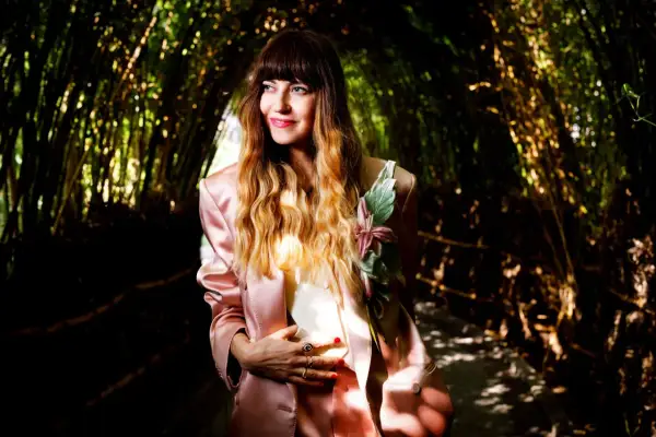 Chiara Tagliaferri, con un tailleur rosa e un fiore sul petto, posa in un tunnel di bambù illuminato dal sole.
