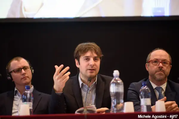 Beniamino Pagliaro parla a un microfono, con altri due uomini seduti al suo fianco.